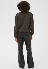 Hnědá mikina vyrobená z měkké tkaniny, spárovaná s černými koženými kalhotami s vysokým pasem a rozšířenými nohavicemi. Důraz na strukturu a barevný kontrast.