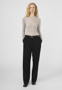 Top bej cu mânecă lungă, cu o textură netedă, asortat cu pantaloni negri cu talie înaltă, prevăzuți cu o curea și buzunare laterale.