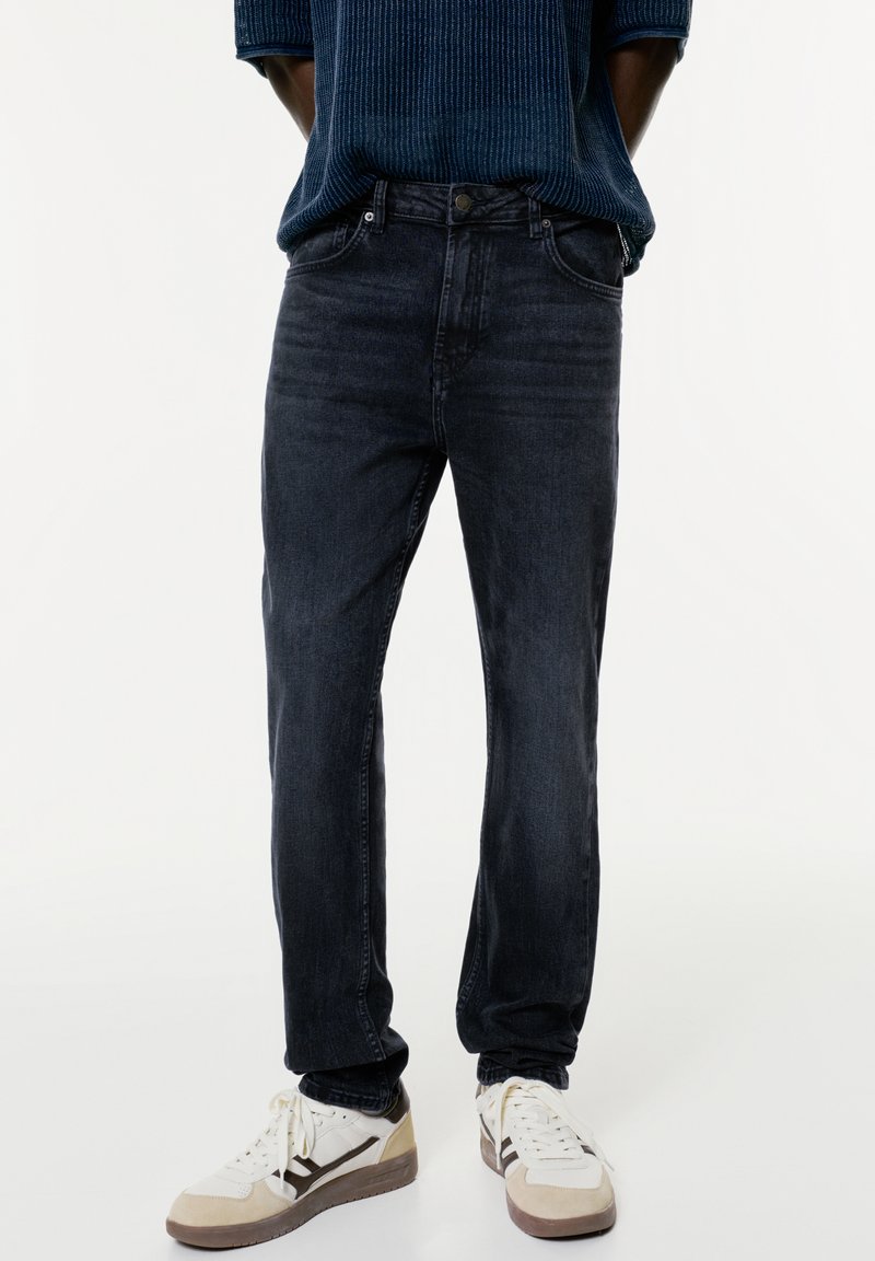 Sötétkék, egyenes szabású farmernadrág, denim anyagból készült. Finom kopásokkal és klasszikus öt zsebes dizájnjal rendelkezik, fehér sportcipőkkel párosítva.
