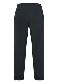 Sorte tilspidsede bukser med elastisk talje og manchetter, med lynlåse ved ankel-sømmene.