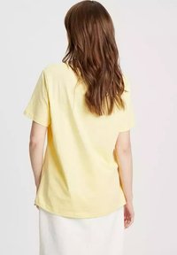 Żółta bawełniana koszulka z krótkim rękawem, luźny krój oraz prosty okrągły dekolt. Gładka tekstura, bez wzorów czy widocznych elementów metalowych.