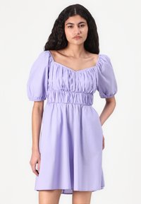 Robe courte lilas avec manches bouffantes, taille élastique et décolleté carré ; texture lisse et détails froncés sur le corsage.