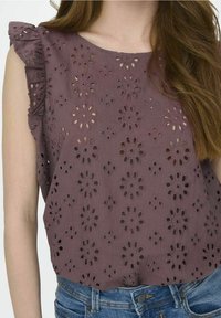 Blusa di cotone viola con design ad occhio di fiori, dettagli con maniche arricciate e una vestibilità ampia, abbinata a pantaloni shorts in denim.