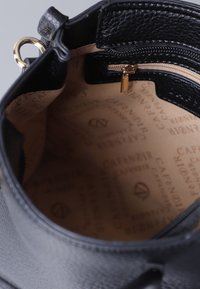 Interno di una borsa in pelle nera con zip dorata, foderato in beige con motivi a logo ripetuti, e una piccola tasca con zip per l'organizzazione.