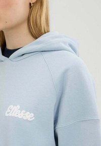 Sudadera azul claro con un gran logotipo bordado en blanco en el pecho, con un dobladillo y puños acanalados, y una capucha con cordón.