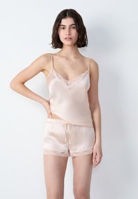 Camisola in raso rosa chiaro con pizzo e spalline regolabili, abbinata a pantaloni corti con orlo in pizzo e vita in raso con coulisse.
