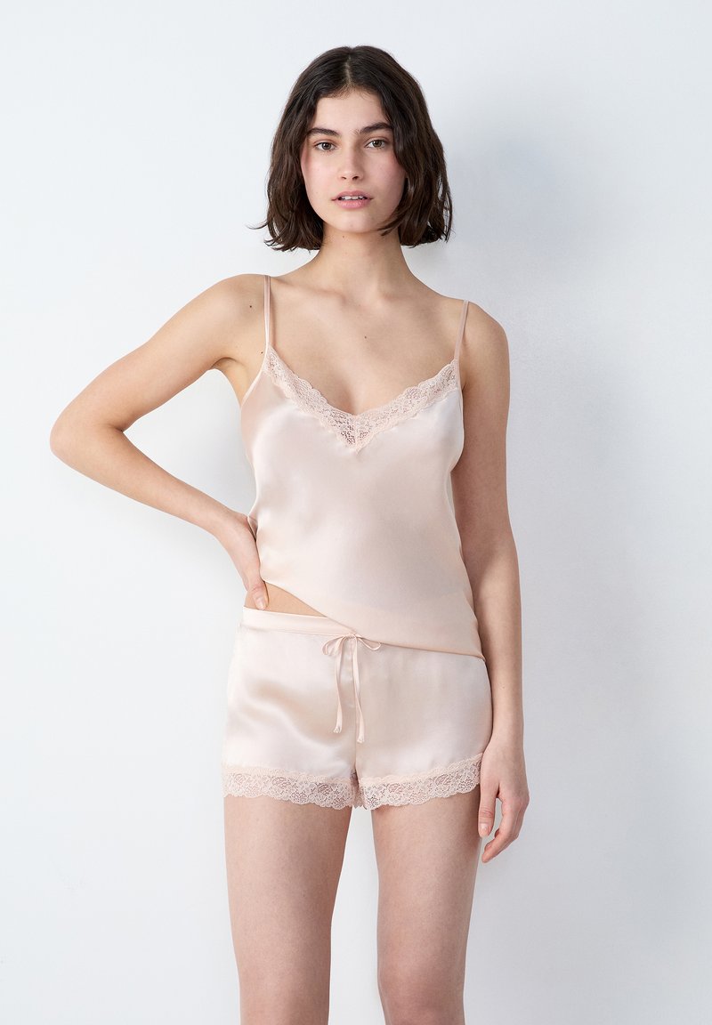 Camisola in raso rosa chiaro con pizzo e spalline regolabili, abbinata a pantaloni corti con orlo in pizzo e vita in raso con coulisse.