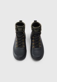 Botas de hiking impermeáveis pretas com colarinhos almofadados verdes e atacadores estampados, vistas de cima sobre um fundo cinza claro.