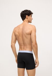 Čierne bavlnené boxerky s svetlomodrým pásom zdobeným logom Calvin Klein, zobrazené zozadu na holom trupe.