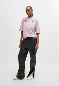 Licht paarse oversized t-shirt met grafische prints, gecombineerd met hoog-gesneden zwarte nep leren broek met drukknopen aan de zijkanten.
