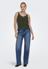 Top de tirantes de punto color verde oliva con patrones florales y dobladillo en forma de concha, combinado con unos vaqueros de tiro alto y pierna ancha de color azul y botas negras de tobillo.