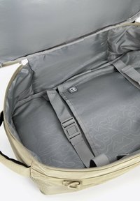 Béžová cestovní taška s šedým interiérem, vybavená nastavitelnými popruhy, hladkým povrchem a jemným vzorem. Hlavní přihrádka na zip.