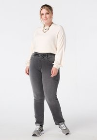 Licht crèmekleurige top met lange mouwen gecombineerd met donkergrijze jeans met elastische taille, zijkantenzakken, omslagen en een ontspannen pasvorm. Casual sneakers maken de look af.