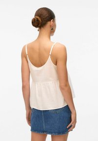 Lys beige peplum top med tynde justerbare stropper og en blød tekstur, båret med en denim mini nederdel med baglommer.