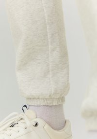 Light gray jogger pants with elastic cuffs, made from soft textured fabric, paired with a white sneaker and light pink sock.