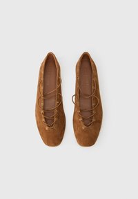 Ballerine in suede marrone con lacci e punta quadrata, viste dall'alto su uno sfondo chiaro.