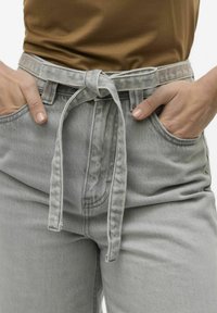 Pantalones de mezclilla grises de talle alto con un cinturón de tela atado en la cintura, que cuentan con bolsillos laterales y un acabado liso y texturizado.