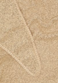 Beige textuurde deken met een zachte, pluizige oppervlakte, met een gladde zoom en subtiel patroon, gedrapeerd en gelaagd.