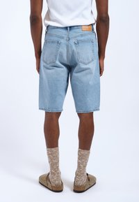 Lichtblauwe denimshorts met een relaxte pasvorm, voorzien van achterzakken en een bruin merklabel. Gecombineerd met gestructureerde, knielange sokken en instappers.