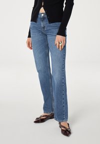 Lichtblauwe spijkerbroek met een recht model, hoge taille en subtiele slijtage-effecten, gecombineerd met puntige, bordeauxrode laarzen van gepatenteerd leer.