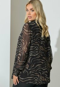 Durchsichtige schwarze Bluse mit einem strukturierten Zebra-Print in Brauntönen und Beige, mit langen Ärmeln und einem geknöpften Bündchen.