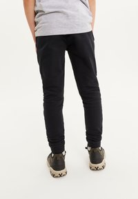 Pantalons noirs ajustés en tissu doux avec une taille élastique, associés à des chaussures de sport marron et noires avec une semelle texturée.