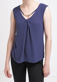 Mörkblå ärmlös topp med djup V-ringning, med veck framtill och en guldaccent vid halsringningen. Lättviktigt tyg.