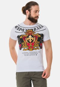 Weißes Baumwoll-T-Shirt mit einem bunten grafischen Design, das ein Wappen, Pantherköpfe, ein Kettenmotiv und Markentext auf der Vorderseite zeigt.