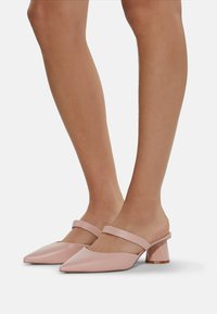 Mules in pelle rosa con punta affusolata e una larga fascia sulla parte superiore del piede; presentano un tacco spesso e trasparente. Texture liscia.