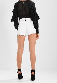 Blusa negra transparente con mangas con volantes, combinada con shorts de mezclilla blancos de talle alto con bordes deshilachados. Botines negros completan el look.