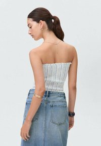 Stribet off-shoulder top i hvidt og blåt stof, parret med en højtaljet denimnederdel. Modellen viser rygvisning, med minimale accessories.