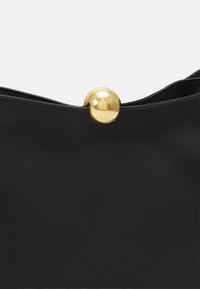 Borsa a tracolla in pelle nera con una chiusura rotonda in oro. Presenta una texture liscia e un design minimalista. Decorata con incisione del marchio.