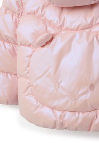 Tessuto trapuntato rosa con un design di faccia d'orso, caratterizzato da occhi, naso ricamati e una piccola orecchia imbottita su un materiale gonfio.
