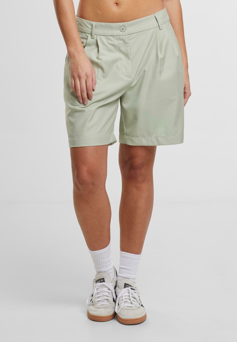 Ljusgröna knälånga shorts med veckad fram, uppvikta fållar och knappstängning. Materialet ser slätt och väldefinierat ut.