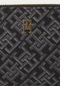 Čierna a sivá textilná peňaženka s geometrickým vzorom a zlatým logom na prednej strane. Zips po vrchu.