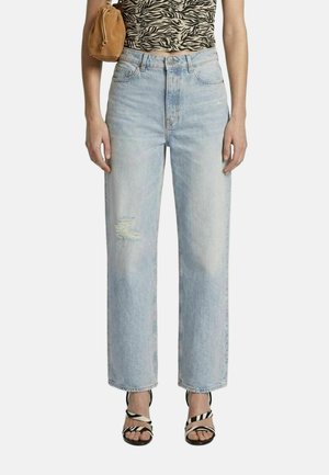 Vrouw draagt lichtblauwe high-waist jeans met een gescheurde knie, zebraprint crop top, bruine schoudertas en zebragestreepte sandalen.