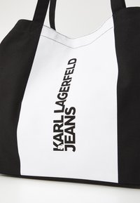 Black and white tote bag featuring the text "KARL LAGERFELD JEANS" in bold black letters, with a canvas texture and contrasting color blocks.