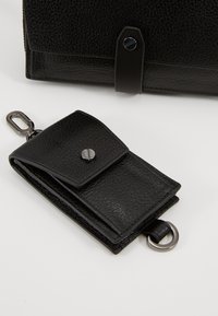 Svart läderplånbok med texturerad yta, med tryckknappslås och metallbeslag, försedd med en nyckelring.