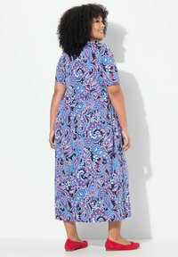 Vestido maxi con mangas cortas en una tela azul marino que presenta un colorido patrón de paisley. Unos zapatos planos rojos complementan el atuendo.