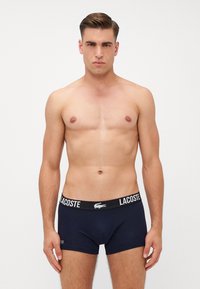Temno modri moški boksarji iz bombaža, z črnim pasom z belim logotipom "LACOSTE" in logotipom krokodila.