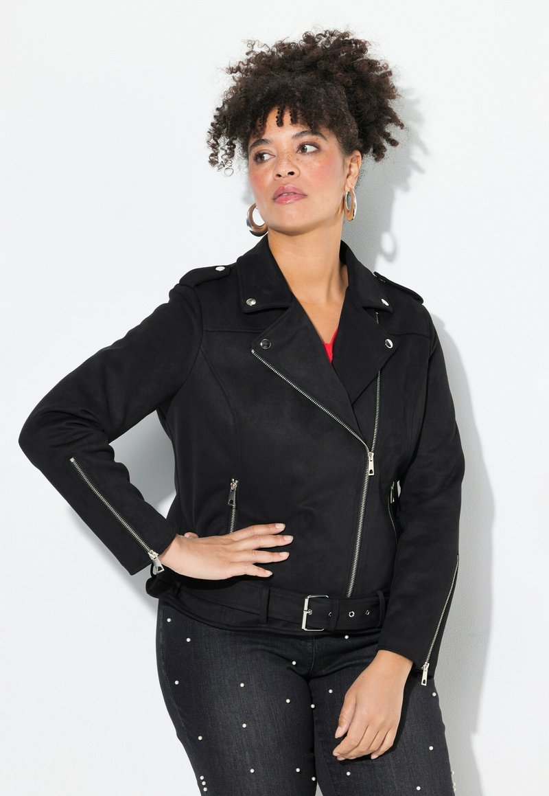 Black faux suede biker jacket with a belted waist, silver zippers, and epaulets. Paired with dark jeans featuring white bead embellishments.