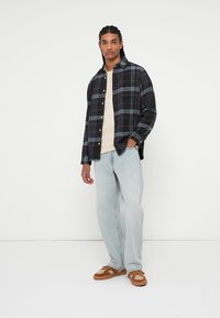Rute flannel skjorte i navy, grøn og grå, lagd over en cremet T-shirt. Lyseblå loose-fit jeans og brune sneakers.