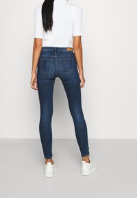 Tajta jeans i mörkblå denim med en mjuk yta, med midjehöjd, bakfickor, och matchade med vita sneakers.