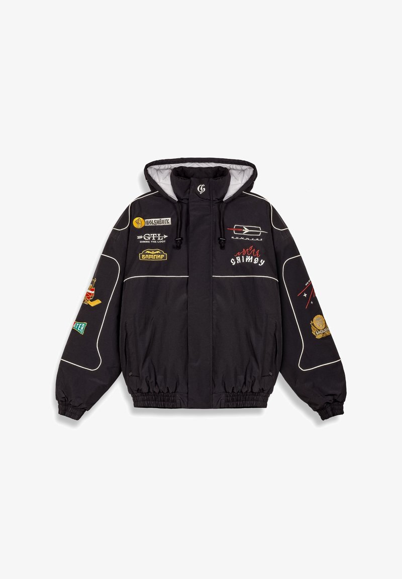 Zwarte jas met een capuchon, voorzien van witte piping, meerdere patches, elastische manchetten en een koord in de hals. Gemaakt van gladde stof.