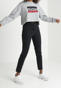 Felpa grigia corta con logo "Levi's", abbinata a jeans neri a vita alta e sneakers bianche. Tessuto liscio, vestibilità comoda e dettagli minimi.