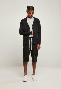 Fekete kötött kardigán, elülső gombokkal, szürke pólóval és zsebes fekete sorttal párosítva. A fehér tornacipő teljesíti a szettet.