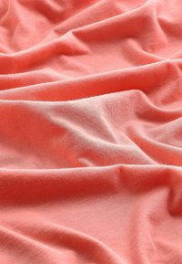 Tissu doux rose corail avec des plis visibles et de douces ombres, créant une surface texturée et légèrement froissée. Aucun personne ou objet présent.