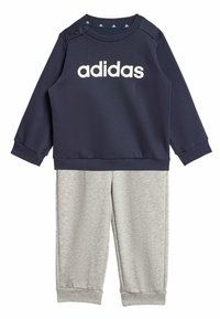 Felpa navy con logo bianco "adidas", dotata di bottoni a pressione sulle spalle; abbinata a pantaloni grigi chiari, entrambi in tessuto morbido e testurizzato.