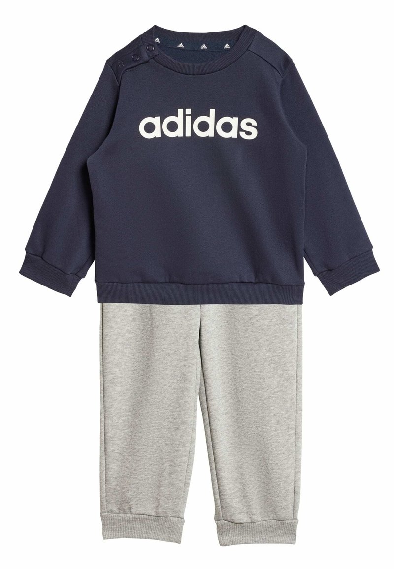 Felpa navy con logo bianco "adidas", dotata di bottoni a pressione sulle spalle; abbinata a pantaloni grigi chiari, entrambi in tessuto morbido e testurizzato.