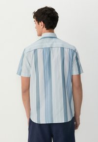 Majica s kratkimi rokavi v svetlo modri in beli vertikalni črtasti vzorec. Narejena iz gladkega materiala, ima ovratnik in ravno spodnji rob.